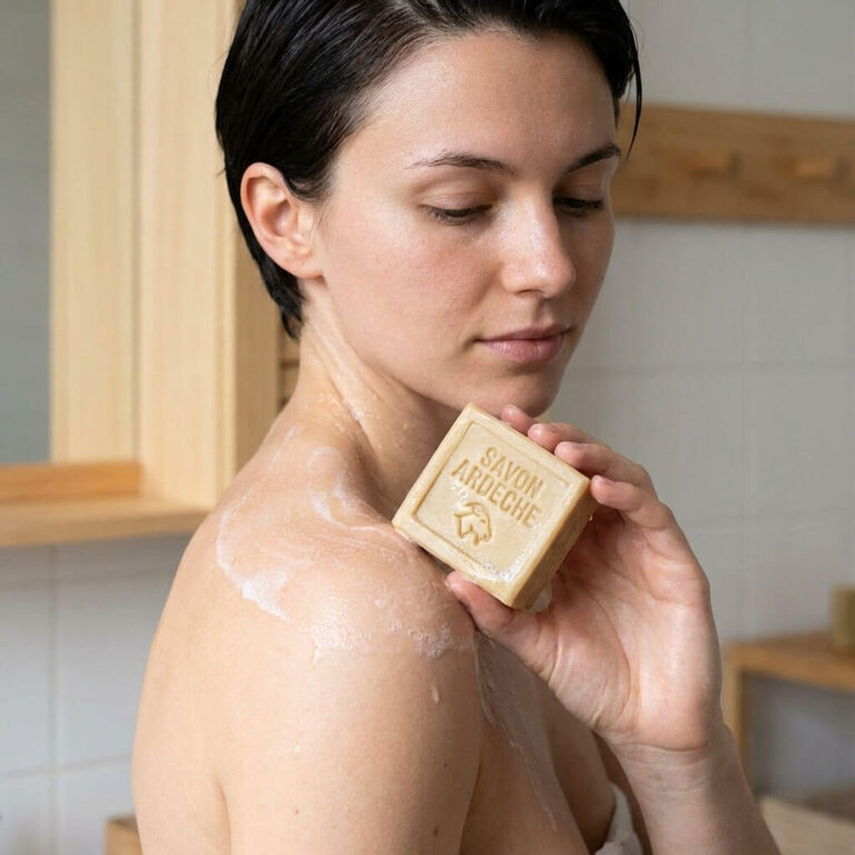 Femme utilisant un savon artisanal au lait de chèvre Savon d’Ardèche sur la peau dans une salle de bain naturelle