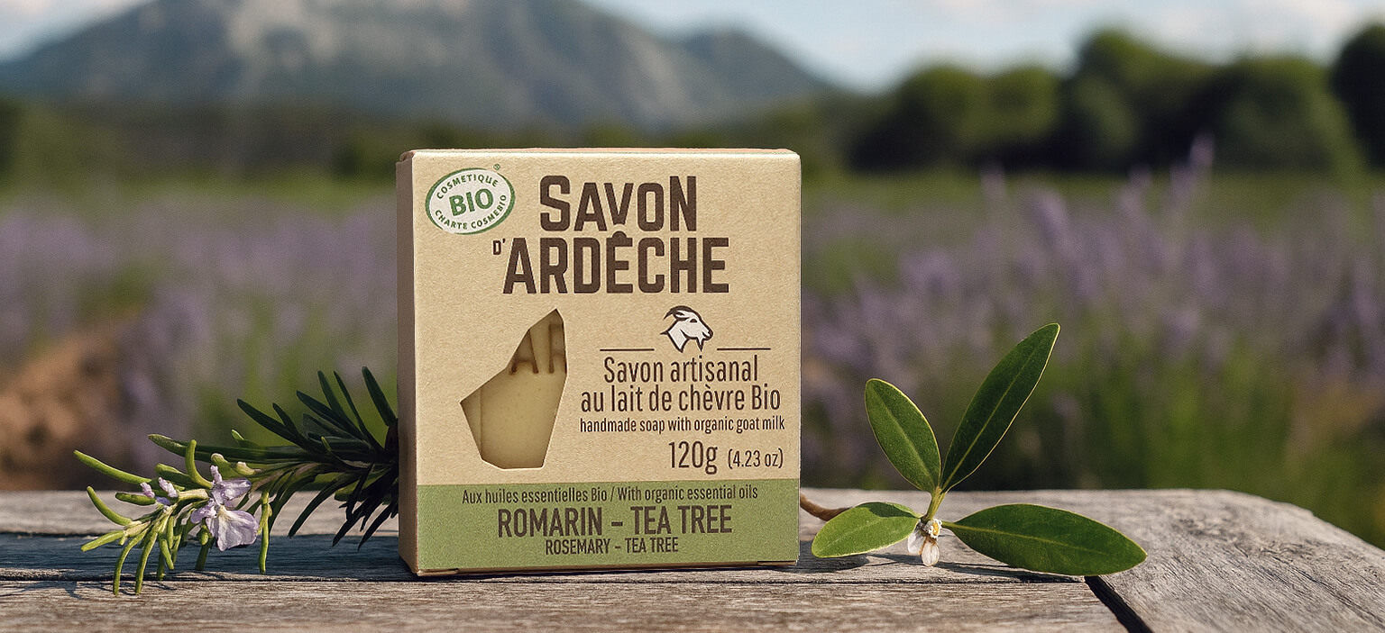 Savon bio au lait de chèvre aux huiles essentielles de romarin et tea tree devant un champ de romarin en fleur