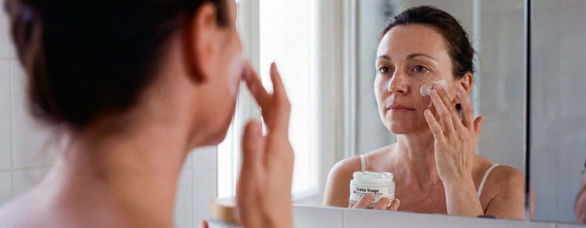 Femme appliquant une crème visage au lait de chèvre Savon d'Ardèche lors de sa routine quotidienne