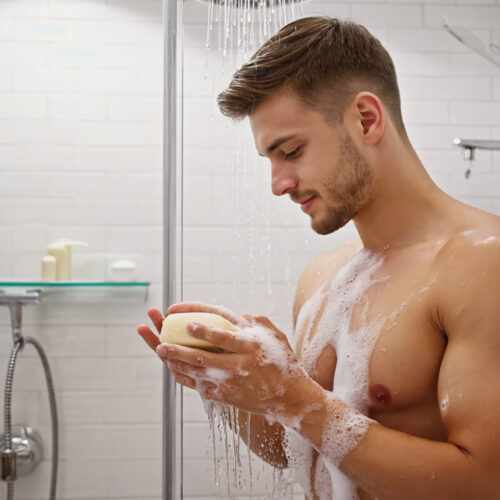 Homme sous la douche se savonnant le corps avec un savon naturel