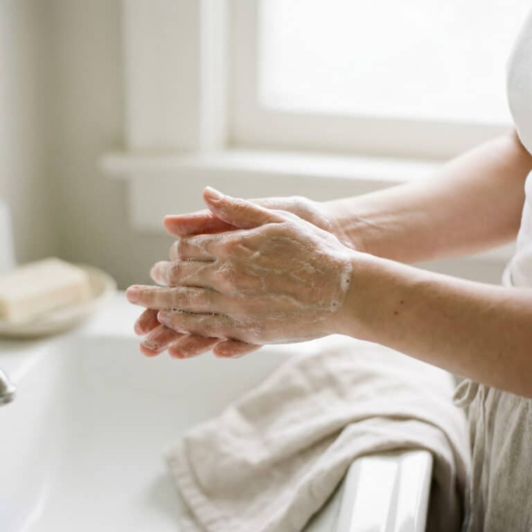 Mains recouvertes d’une mousse fine lors du lavage avec un savon au lait de chèvre dans une salle de bain lumineuse.